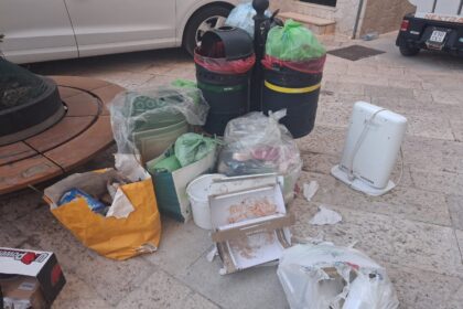 Foto dei rifiuti abbandonati in piazza San Paolo ad Acquaviva delle Fonti con sacchi e cartoni vicino ai cestini.